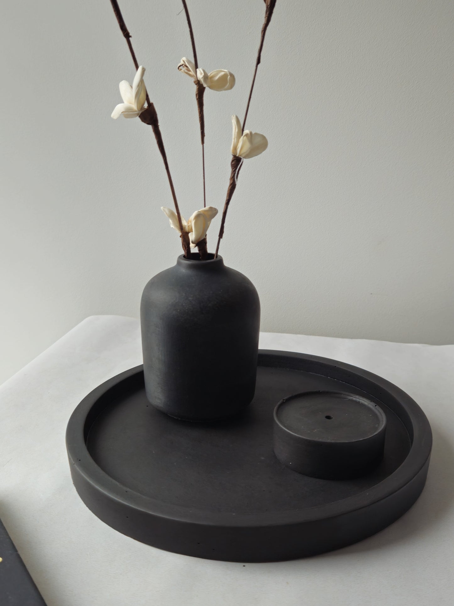 juodas betoninis padėklas su vazele ir smilkaline