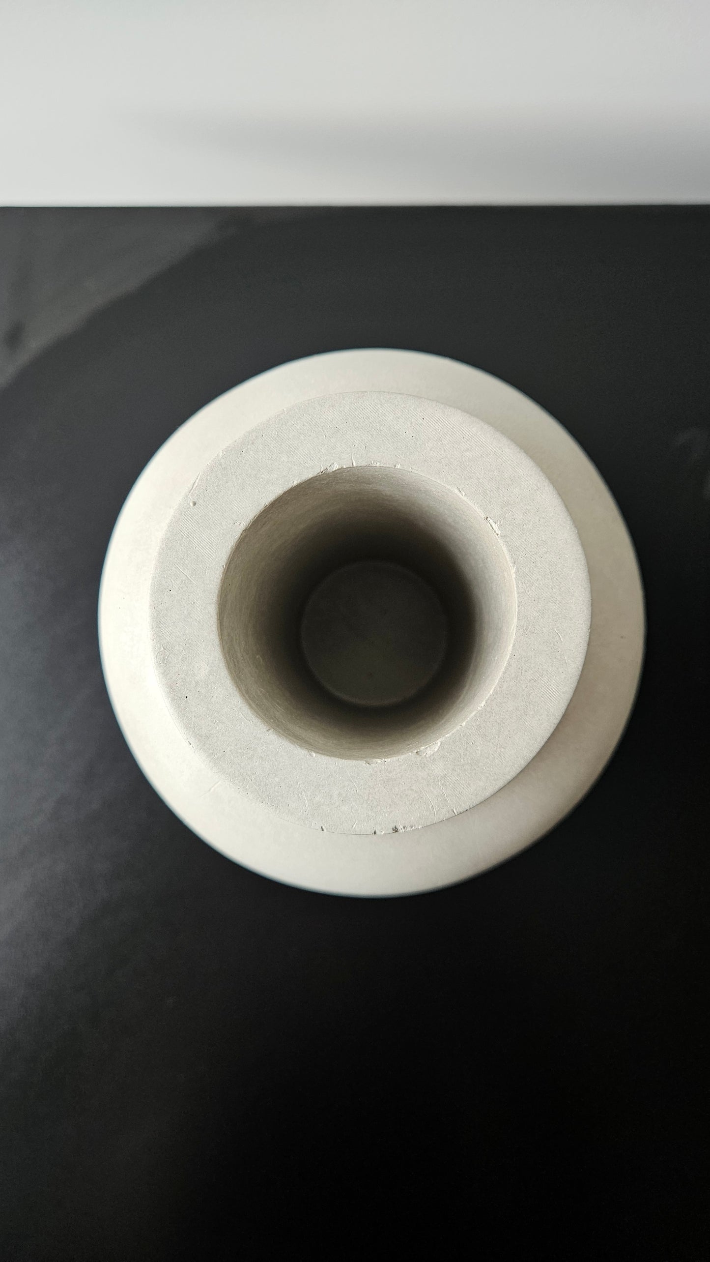 betoninė vaza iš viršaus ant juodo paviršiaus