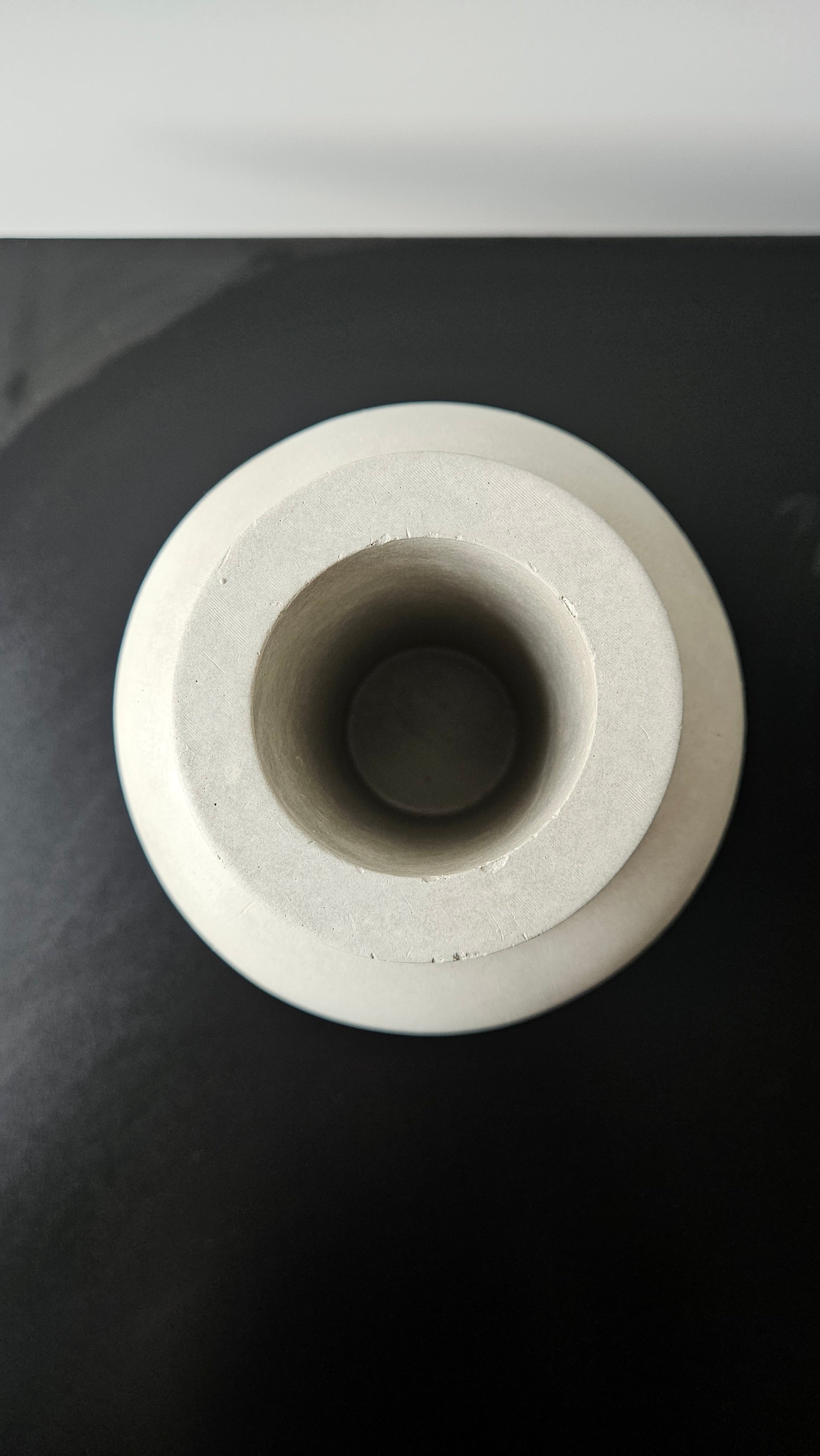 betoninė vaza iš viršaus ant juodo paviršiaus