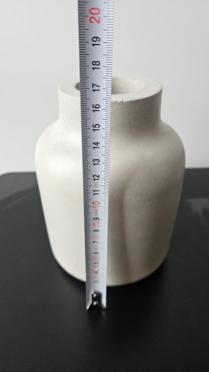 betoninė vaza ant juodo paviršiaus baltame fone su matavimo juosta