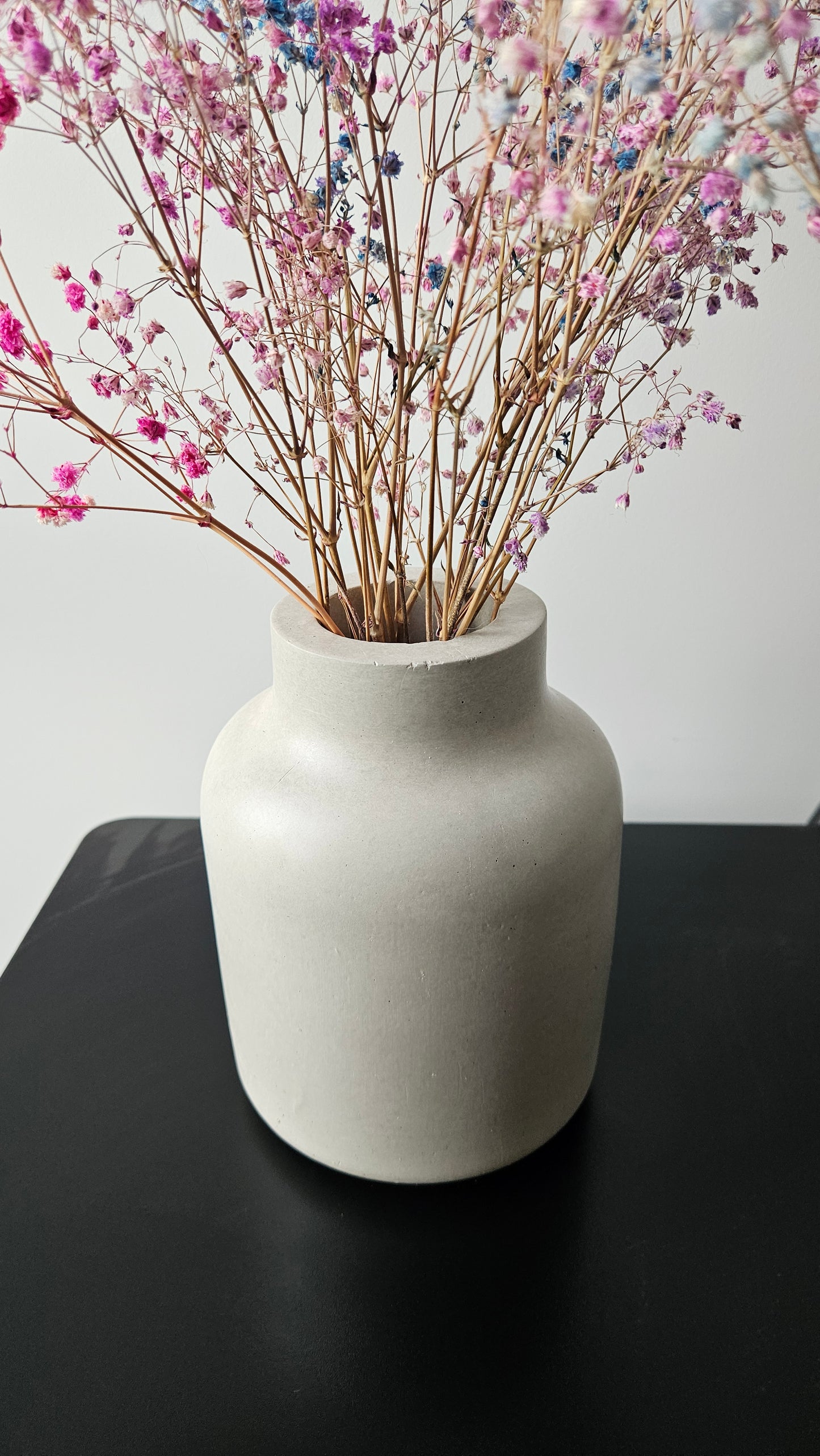 betoninė vaza ant juodo paviršiaus baltame fone