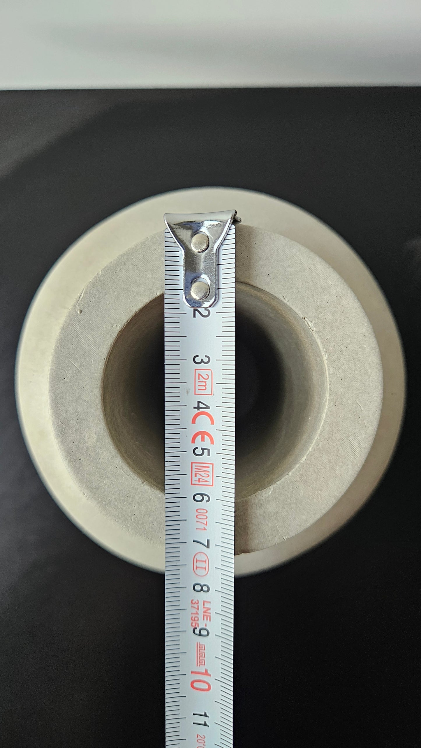 betoninė vaza ant juodo paviršiaus baltame fone