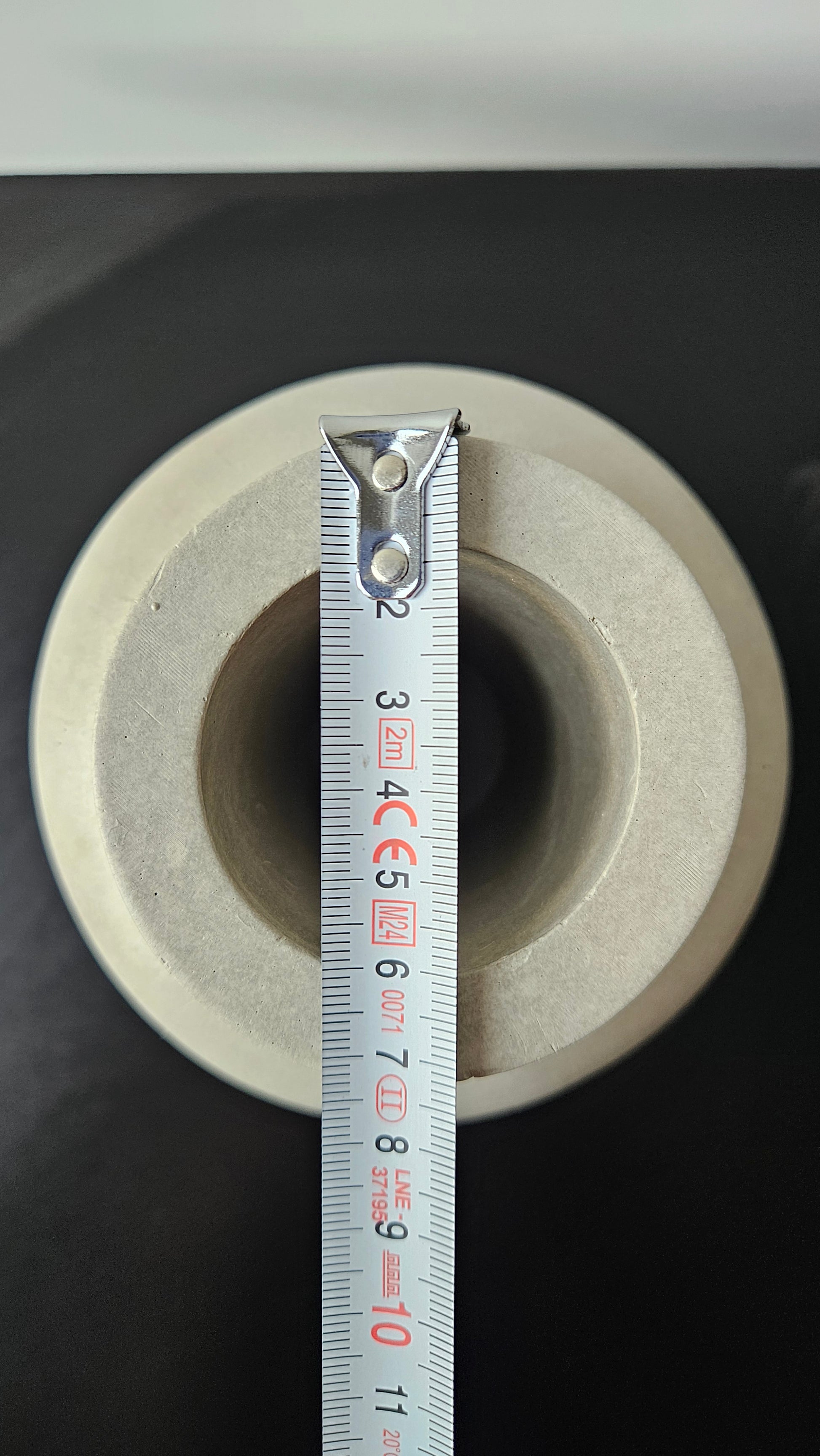 betoninė vaza ant juodo paviršiaus baltame fone