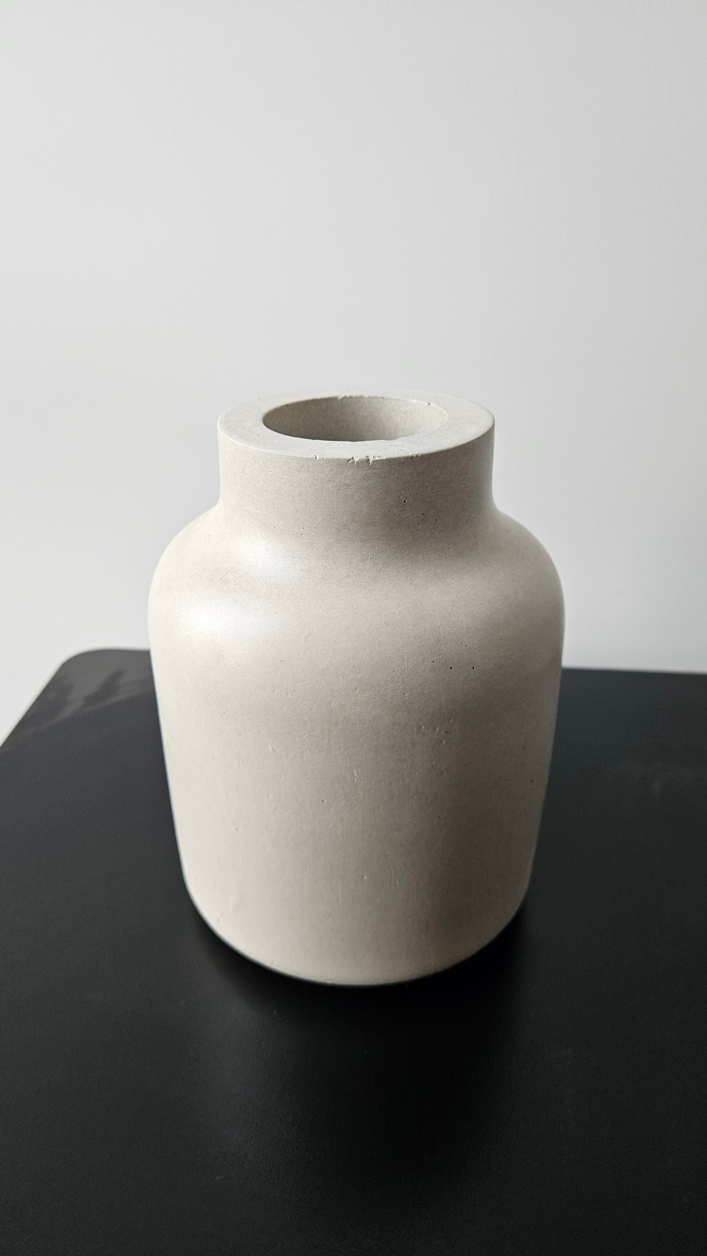 betoninė vaza ant juodo paviršiaus baltame fone