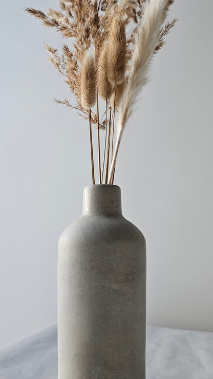 Concrete bottle with dried pampas grass against a light background
