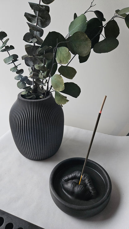 Rankų darbo juoda rumbuota betoninė vaza su auksinėmis šakomis ir žaliais lapais, skirta moderniam ir minimalistiniam interjerui.