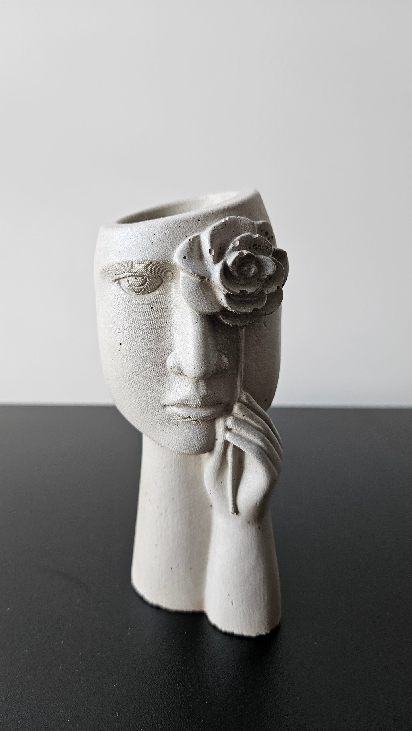 Minimalistinė rankų darbo betono vaza veido skulptūros formos, dekoruota rože