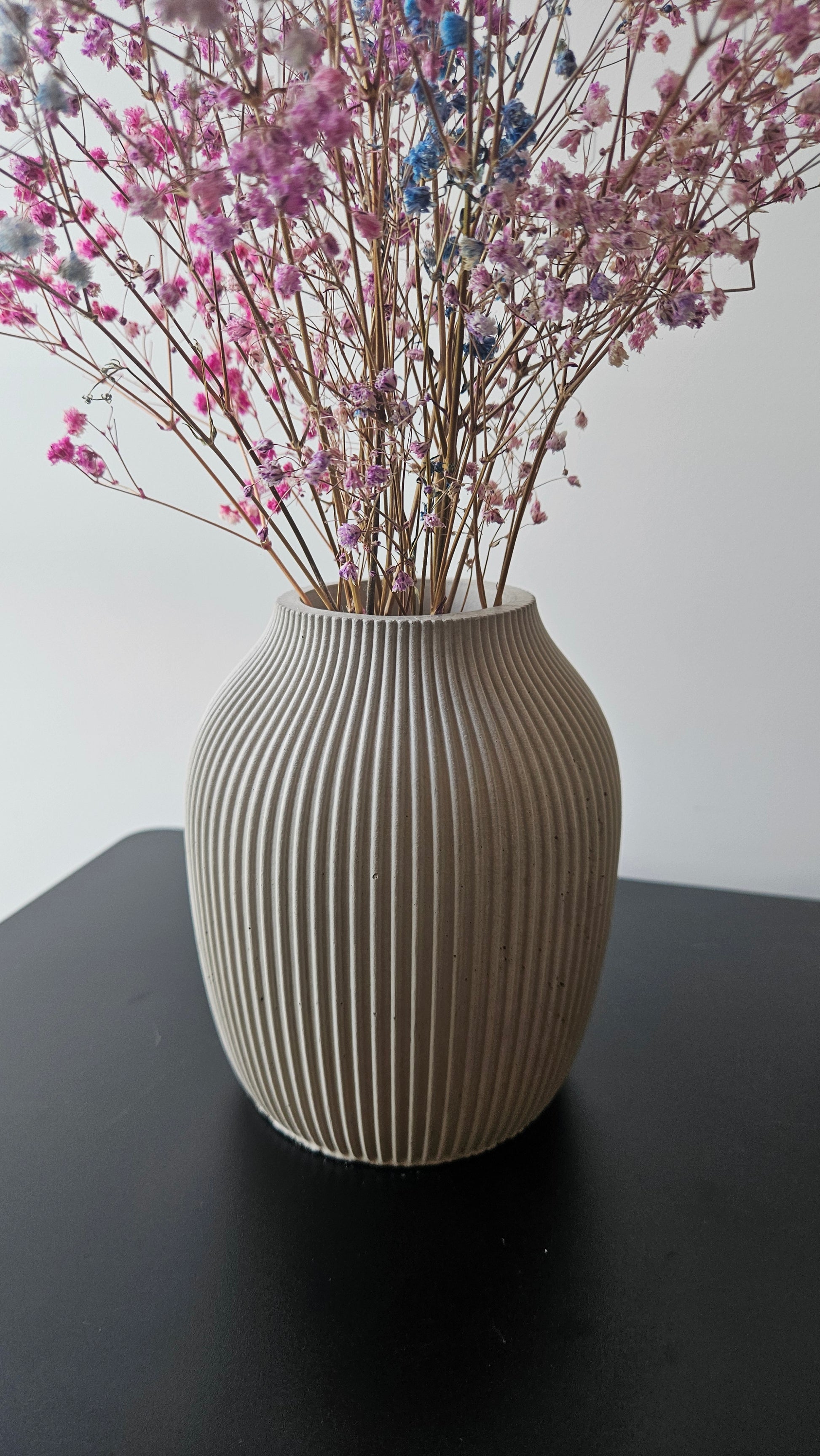 Decorative vase with ribbed texture holding pink and blue flowers on a white surface.