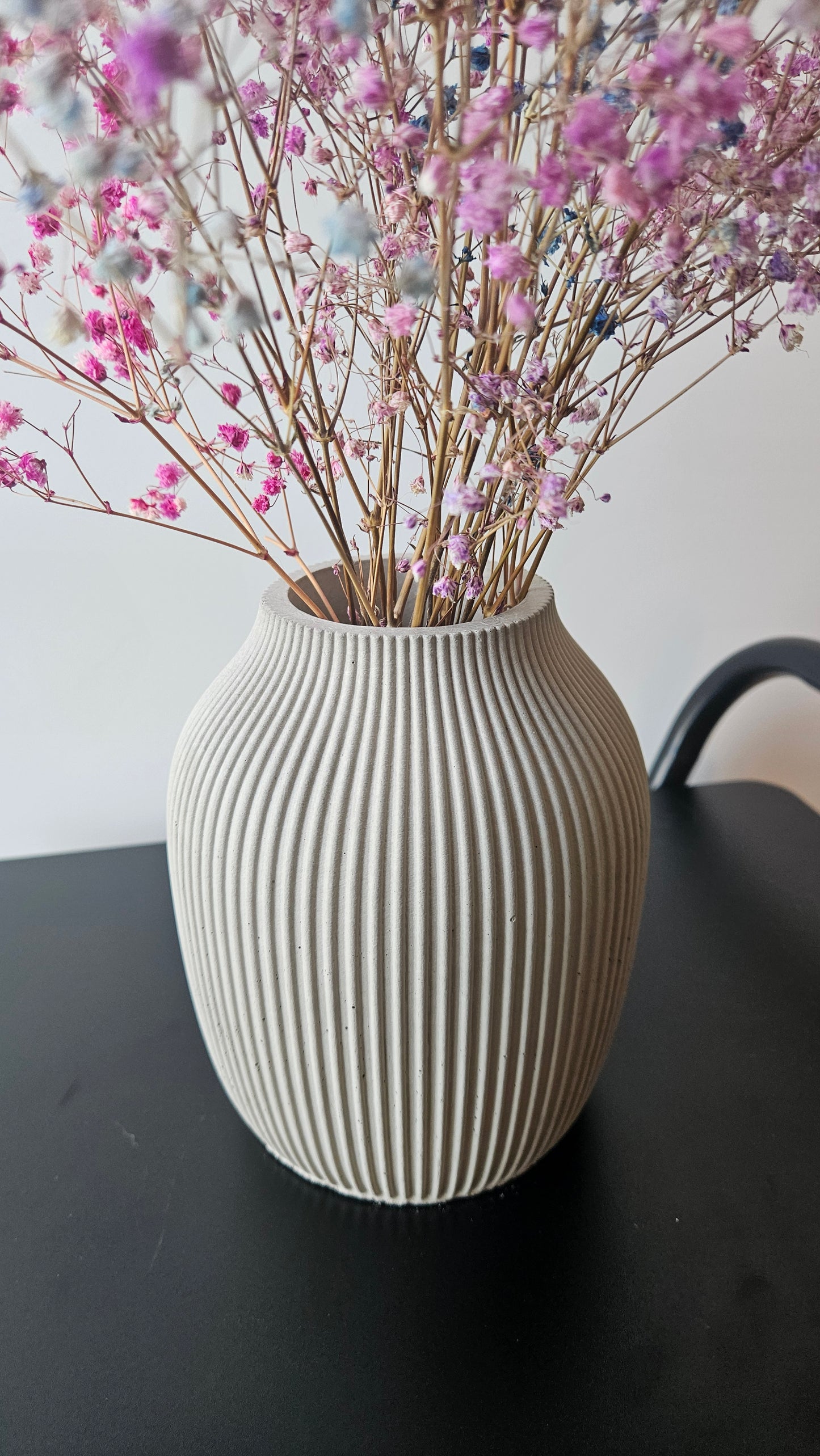 Decorative vase with ribbed texture next to pink flowers on a light surface.