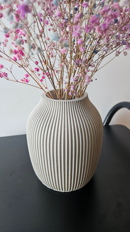 Decorative vase with ribbed texture next to pink flowers on a light surface.