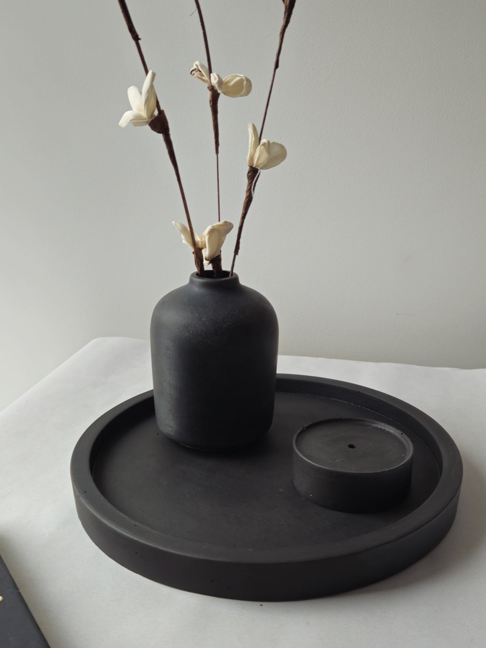 juodas betoninis padėklas su vazele ir smilkaline